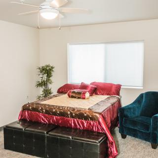 A cozy bedroom with red bedding, a teal armchair, and a potted plant near the window.
