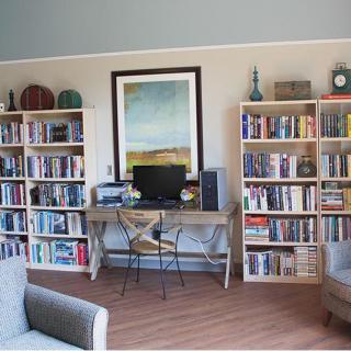 A cozy home office space featuring bookshelves filled with books, a desk with a computer, and a comfortable seating area.