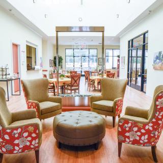 A spacious and elegant seating area with four chairs around an ottoman, leading into a bright dining space.