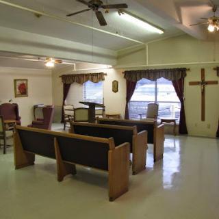 A serene interior of a chapel with wooden seating and a prominent cross on the wall.
