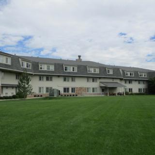 A large residential building with a well-maintained green lawn in front, set against a partly cloudy sky.