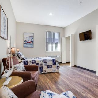A modern hotel bedroom with a queen bed, armchairs, and a wall-mounted television.