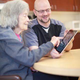 A caregiver assists an elderly woman as they explore a tablet together, sharing a moment of connection and learning.