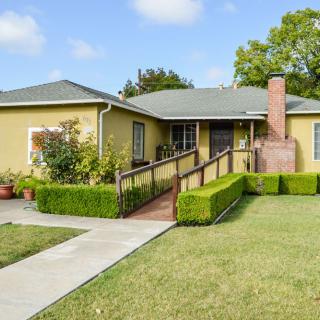 A suburban house with a ramp leading to the entrance, surrounded by a well-maintained lawn and garden.