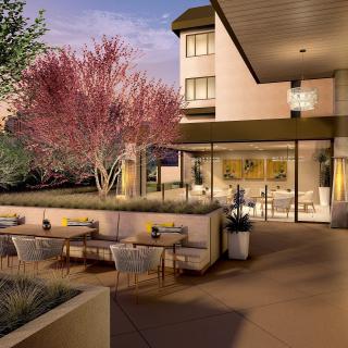 A modern restaurant patio with outdoor seating, set against a backdrop of trees during the evening.