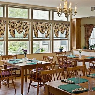 A cozy dining room with neatly arranged tables and chairs, featuring decorative window treatments and a chandelier.