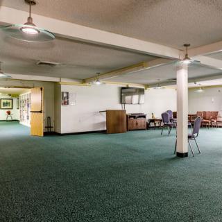 A spacious basement room with green carpet, pillars, and scattered furniture.