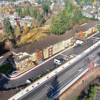 An aerial view of a newly constructed building adjacent to a road with surrounding trees and urban landscape.