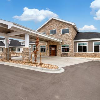 A modern residential building with a stone facade and a spacious driveway under a clear blue sky.