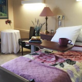 A cozy hospital room with a bed, nightstand, and a floral blanket.