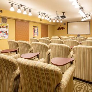 A cozy small theater room with multiple rows of plush armchairs facing a large projection screen, illuminated by overhead lights.