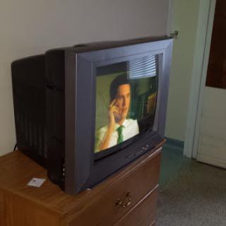 A vintage television set displaying a scene, placed on a wooden dresser in a cozy room.