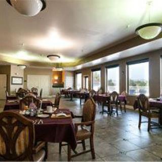 A spacious dining room with neatly arranged tables and chairs, large windows, and ambient lighting.