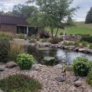 A serene garden with a tranquil pond surrounded by lush greenery and decorative stones.