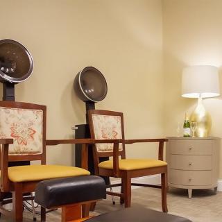 A cozy salon interior with chairs and built-in hair dryers, complemented by a lamp and side table.