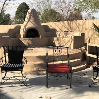 A cozy outdoor seating area featuring three chairs around a charming fireplace.