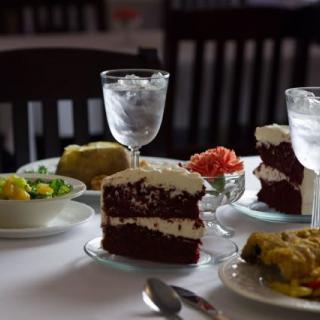 A beautifully set dining table featuring slices of red velvet cake, salad, and glasses of water.