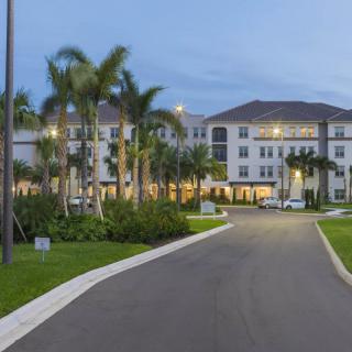 A well-lit building surrounded by palm trees, viewed during the evening.
