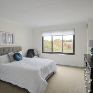 A bright and cozy bedroom with a large window, a neatly made bed, and simple decor.