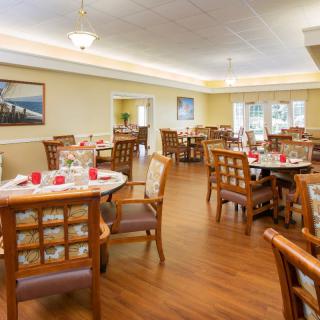 A well-arranged dining room with neatly set tables and comfortable chairs, featuring warm lighting and wood flooring.