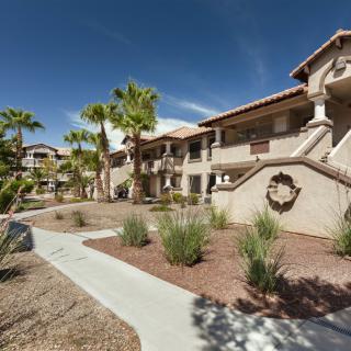 A southwestern-style apartment complex with palm trees and a desert landscape under a clear blue sky.