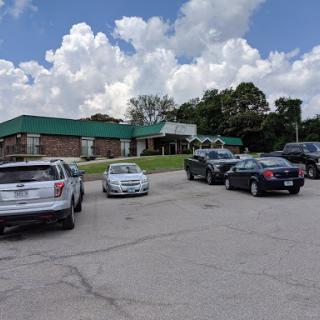 A view of a building with a green roof and several cars parked in the lot under a partly cloudy sky.