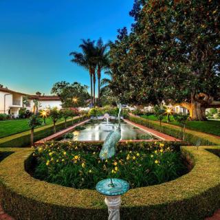 A beautifully landscaped garden with a central fountain surrounded by hedges and flowers, set against an evening sky.
