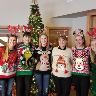 A group of people wearing festive Christmas sweaters standing in front of a decorated tree.