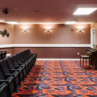 An empty theater room with rows of black chairs and colorful carpet.