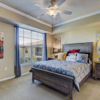 A cozy bedroom with a large bed, ceiling fan, and a window with curtains.