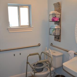 An accessible bathroom equipped with a commode chair and safety grab bars.