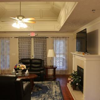 A cozy living room with a couch, coffee table, fireplace, and TV, featuring a ceiling fan and decorative elements.