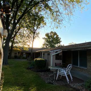 A serene evening scene in a residential area, with trees and patio chairs basking in the warm glow of the setting sun.