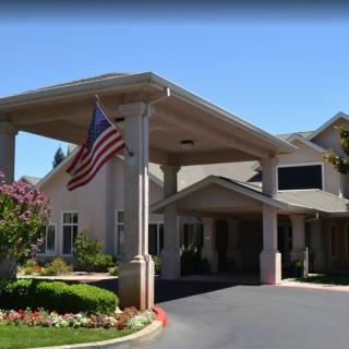 A building entrance with a covered driveway and an American flag, surrounded by well-maintained landscaping on a sunny day.