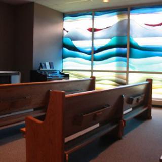 Interior of a church featuring wooden pews and a stained glass window.