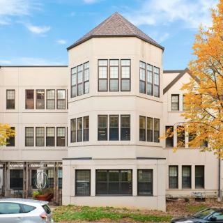 A residential building with a unique architectural design featuring a central tower and large windows, surrounded by autumn foliage and parked cars.
