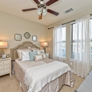 A cozy and elegantly decorated bedroom featuring a neatly made bed, two bedside lamps, and large windows with sheer curtains.