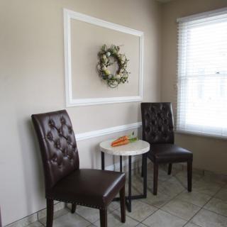 A cozy corner with two dark chairs and a small round table, adorned with a decorative wreath on the wall.