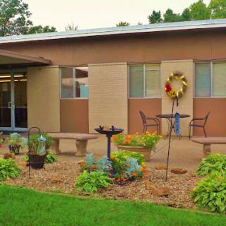 A serene garden area in front of a building, featuring decorative plants and outdoor seating.