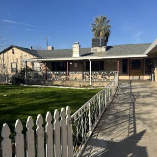 A charming single-story house with a white picket fence and a palm tree in the front yard.