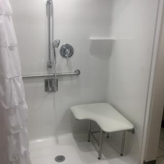 A bathroom with an accessible shower featuring a foldable bench and grab bar.