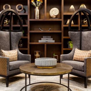 A stylish lounge area featuring two high-back chairs, a round coffee table, and a backdrop of neatly arranged bookshelves with decorative items.