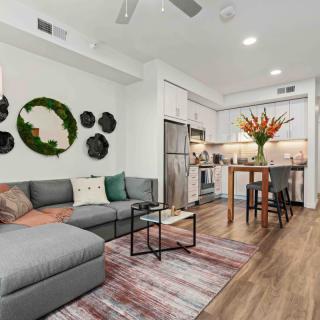 A modern open-concept living room and kitchen area, featuring an L-shaped sofa, wooden flooring, and stylish decor.
