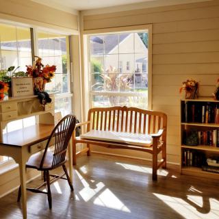 A cozy sunlit room with wooden furniture and a bookshelf, offering a peaceful window view.