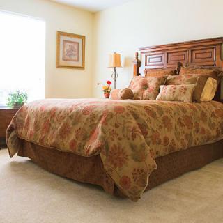 A cozy bedroom with a large wooden bed, decorative pillows, and a bedside lamp.