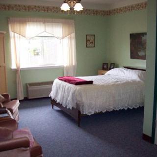 A cozy bedroom with a large bed, carpeted floor, and natural light from a window.