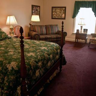 A cozy bedroom with traditional decor, featuring a large bed, lamps, a sofa, and a window.