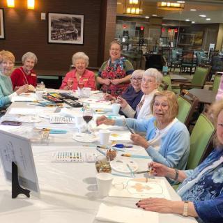 A group of senior women enjoying a painting class together indoors.