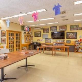 A classroom with tables, chairs, colorful decorations hanging from the ceiling, and posters on the yellow walls.