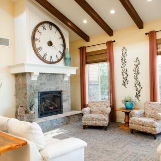 A cozy living room featuring a stone fireplace and a large wall clock, complemented by comfortable armchairs and wooden ceiling beams.